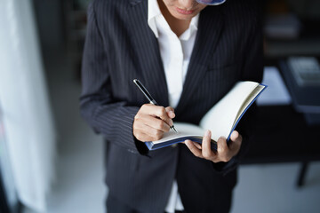 Asian businesswoman in suit standing using pen writing on notebook
