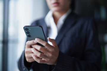 Asian businesswoman in suit standing using smartphone checking email