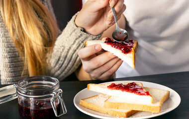 Young guy and his girlfriend having toasts with jam and coffee for breakfast in kitchen