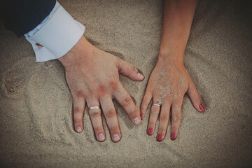 close up of  bride and groom holding hands on a sand,