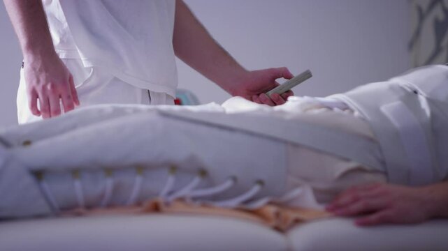 Healthcare professional adjusting the height of a patient's hospital bed using a remote control during a compression therapy session. Concept of rehabilitation, advanced medical care and comfort