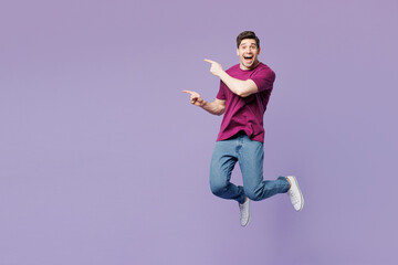 Full body young Caucasian man wear violet t-shirt casual clothes jump high point index finger aside on area mock up isolated on plain pastel light purple background studio portrait. Lifestyle concept.