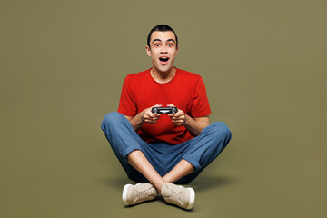 Full body surprised young middle eastern man he wear red t-shirt casual clothes sits hold in hand play pc game with joystick console isolated on plain pastel green background studio Lifestyle concept © ViDi Studio