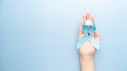 World diabetes day awareness concept. Hands holding blue ribbon with blood drop symbol for diabetes. Support for the fight against diabetes.