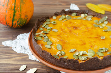 Orange pumpkin pie with dried seeds on a ceramic plate on a wooden table. Rustic style. Autumn mood. Tea time. Horizontal orientation