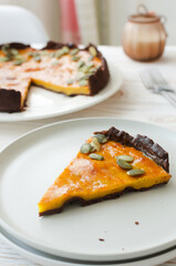 A piece of orange pumpkin pie with dried seeds on a white plate on the table. Autumn mood. Tea time concept. Vertical orientation.