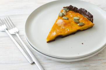 A piece of orange pumpkin pie with dried seeds on a white plate with forks on the table. Autumn mood. Tea time concept. Horizontal orientation