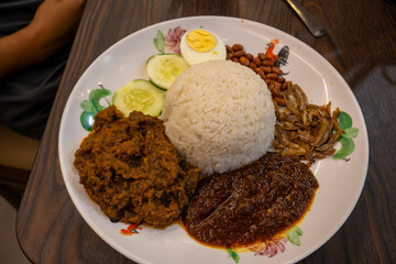 A delicious plate of Nasi Lemak, a popular Malaysian dish, featuring fragrant coconut rice, spicy sambal, fried anchovies, peanuts, cucumber, and a hard-boiled egg. 