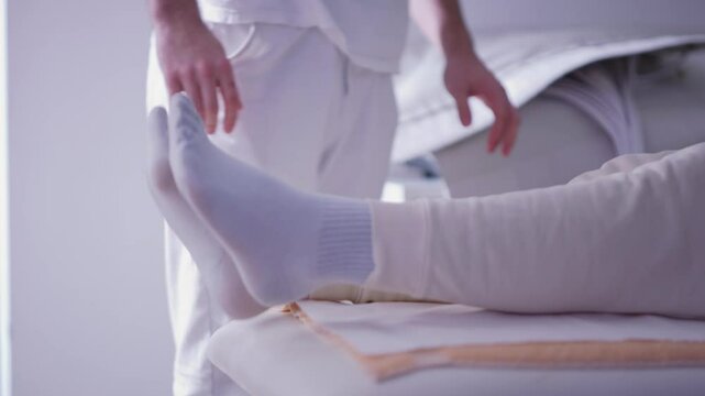 Male patient undergoing preparation for pneumatic compression therapy in a medical facility. The footage highlights rehabilitation equipment and hands-on care. Concept of health recovery and wellness
