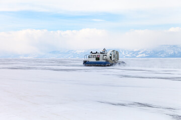 Baikal Lake in winter. Tourists travel on ice of frozen Small Sea on boats on air cushions Hivus in february snowy day. Beautiful winter landscape. Natural background. Ice travel and adventure