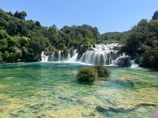 Fototapeta premium Breathtaking Waterfall Cascading into Crystal Clear Waters Surrounded by Lush Greenery