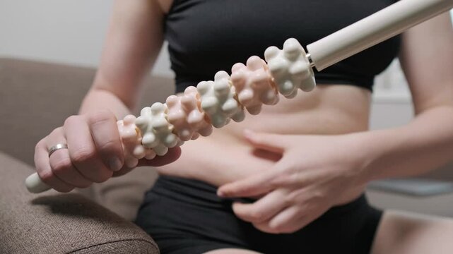 Overweight woman using a wooden massager on her abdomen, massaging to reduce weight and cellulite.