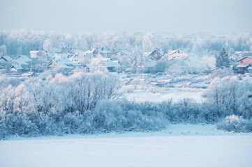 Winter rural background, rural buildings covered with snow, winter evening view with countryside houses near the frozen river, peaceful winter rural landscape