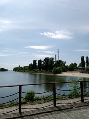 Obraz premium A serene riverside view on a sunny day with trees along the bank and distant industrial structures in the background
