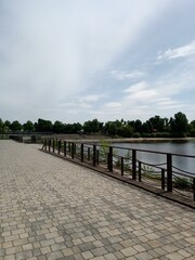 Fototapeta premium A peaceful walkway by the serene lake surrounded by lush greenery under a clear sky in the afternoon light