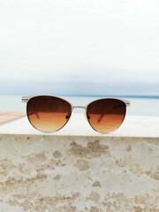 Sunglasses resting atop a stone ledge with a serene ocean view in the background against a cloudy...