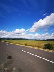 Fototapeta premium A picturesque country road under a bright blue sky with fluffy clouds and lush green fields in the distance during a sunny day