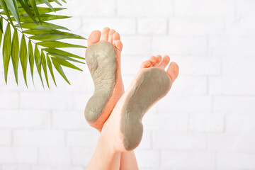 Beauty care in spa. Foot care with clay on white brick wall, with palm leaves, close up, free space