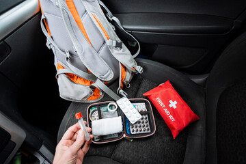 A person is currently holding a syringe adjacent to a first aid kit that is located inside a car. This scenario suggests an emergency situation that may require immediate assistance