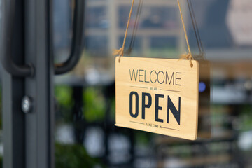 A wooden sign hanging from a window that says "Welcome" and "Open"