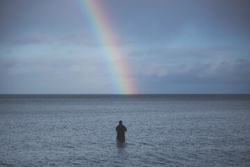 Fisherman Standing in Shallow Water with a Vibrant Rainbow Touching the Horizon