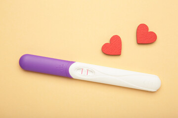 The positive pregnancy test with heart on beige background. Test strip which shows the positive result. Top view