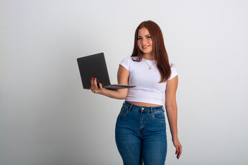 a pretty Student with a laptop wearing a white shirt and jeans posing smiling and looking at the camera, medium large portrait