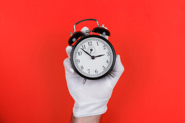 Gloved Hand Holding Black Alarm Clock on Red