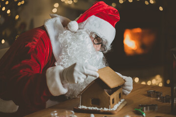 Jolly Santa Claus baking ginger bread, making ginger bread house. Warm and cozy festive room with...
