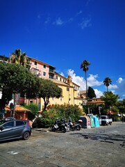 Colorful buildings and palm trees line the sunny square in a charming coastal village during midday