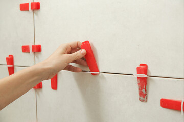 Woman tiling bathroom walls. Flat wall plastic tile leveling system. Process of installation of...