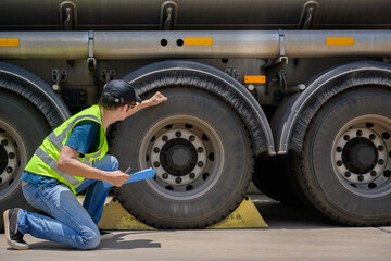 A safety inspector inspects the tires of a big fuel tanker while wearing a reflective vest. He...