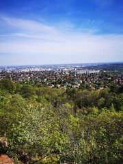 A panoramic view of a sprawling city nestled among green hills under a clear blue sky during a...