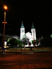 Beautiful illuminated church at night surrounded by trees in a lively city square during the...