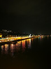 Night view of a vibrant riverfront with illuminated pathways and reflections under the city lights...