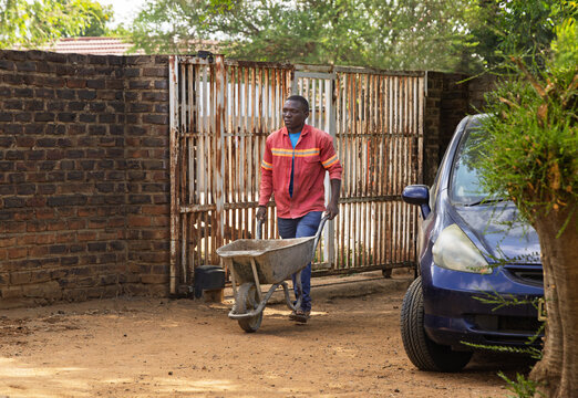 african construction worker gardener with a wheelbarrow cleaning rubble and garbage in a yard