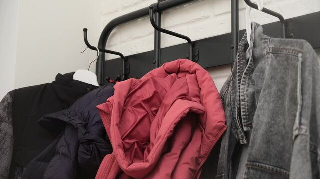 Hand reaching for red winter jacket on coat rack with various colorful jackets hanging on hooks. Indoor clothing organization concept.