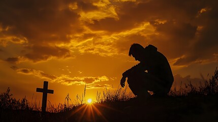Silhouetted person mourning at grave cross against dramatic orange sunset sky, copy space