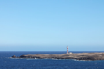 On a headland stands this lighthouse isolated. Red and white striped with sea as background