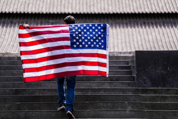 Young man proudly holds an American flag while standing on steps, symbolizing patriotism and pride. The flag's vibrant colors contrast with the subdued background, emphasizing national pride.