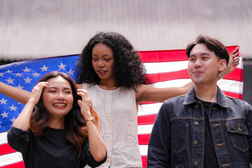 Diverse group of friends proudly holding an American flag outdoors, symbolizing unity and patriotism. Their smiles and casual poses embody freedom, friendship, and the spirit of togetherness.