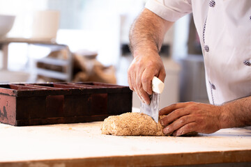 Close up of unrecognizable man cutting dough for fresh bread in bakery, copy space. Man cutting dough at wooden table in kitchen, closeup.