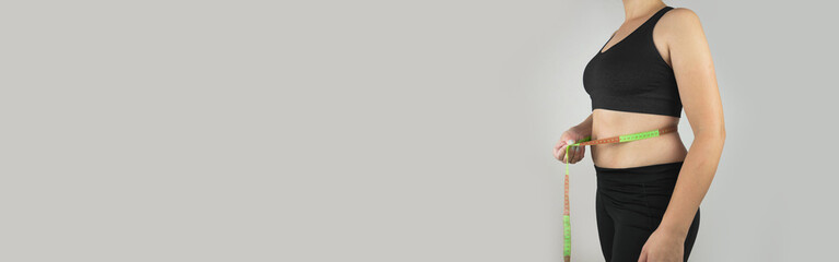 Lose belly fat concept from close up woman in sportswear with hand holding her own belly fat and cellulite. web banner size.