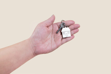 A woman's hand holds keys with a metal keychain in the form of a house on a light background