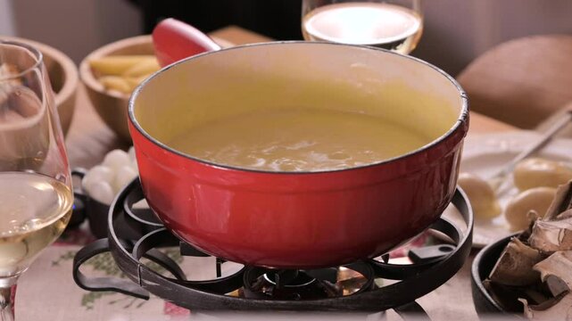 Cozy Swiss fondue setup with melted cheese, bread, pickles, and wine on a rustic table. advertising, social media campaigns, or food-related promotions. High quality 4k footage