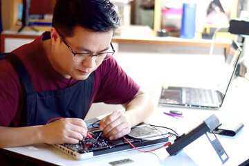 Fototapeta premium Computer technician wearing glasses A laptop motherboard repairman is using an IC meter to find faults on the motherboard to repair on his table. Board repair using modern technology