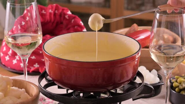 Cozy Swiss fondue setup with melted cheese, bread, pickles, and wine on a rustic table. advertising, social media campaigns, or food-related promotions. High quality 4k footage
