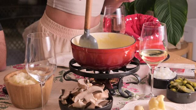 Cozy Swiss fondue setup with melted cheese, bread, pickles, and wine on a rustic table. advertising, social media campaigns, or food-related promotions. High quality 4k footage