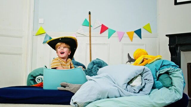 Happy boy in pirate hat having fun among imaginary blanket ocean