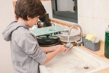 A young boy washes cutlery in a marble sink.